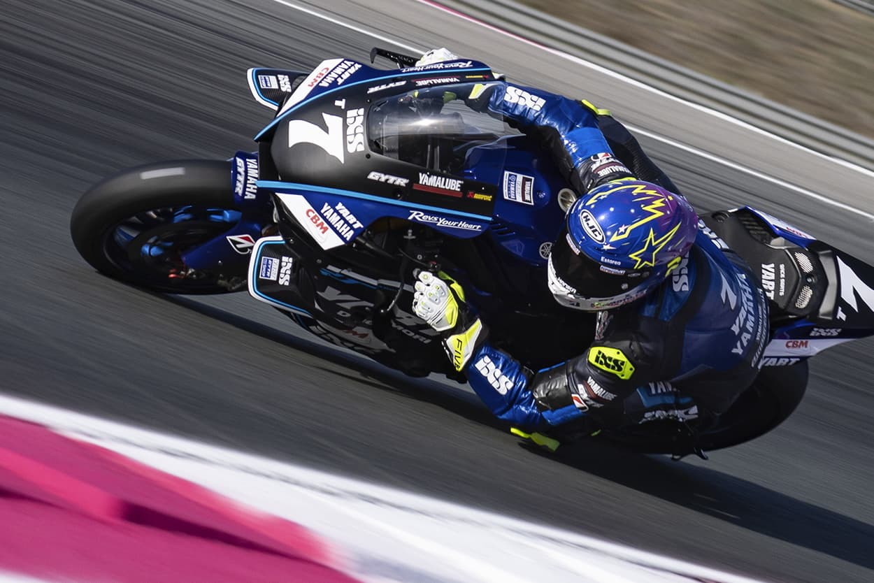 Professional motorcycle racer leaning into a corner wearing white FIVE racing gloves and a colourful HJC helmet on a Yamaha track bike