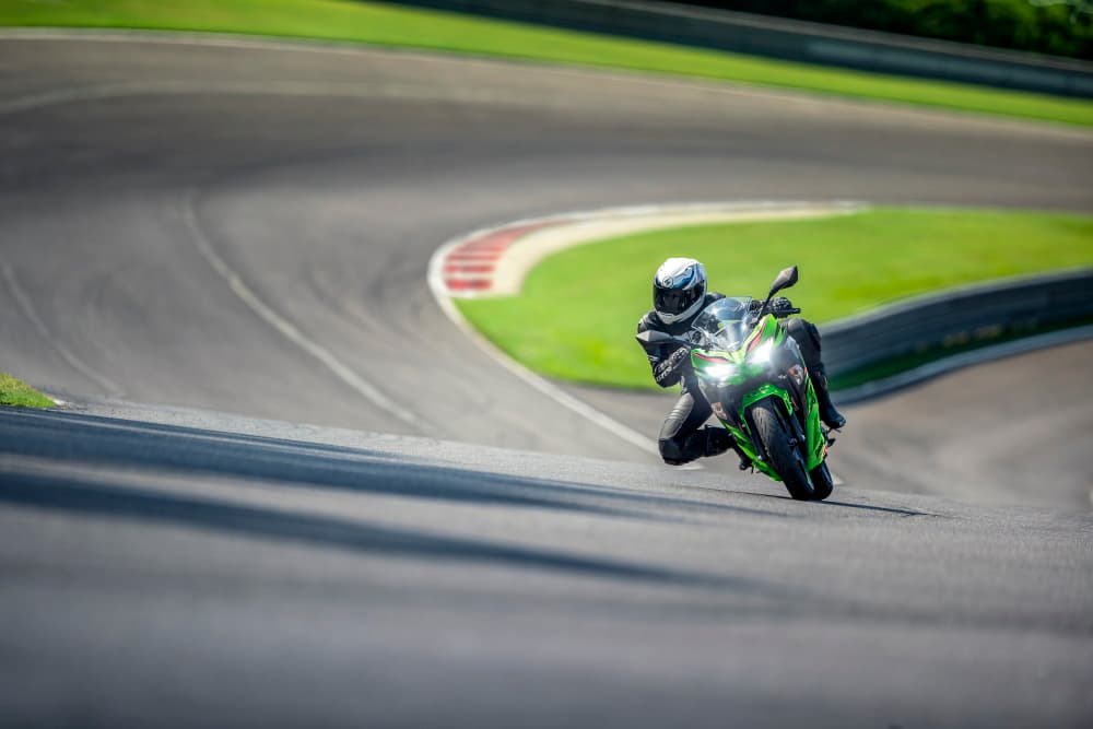 Rider on a lime green Kawasaki Ninja sport motorcycle leaning aggressively into a racetrack corner