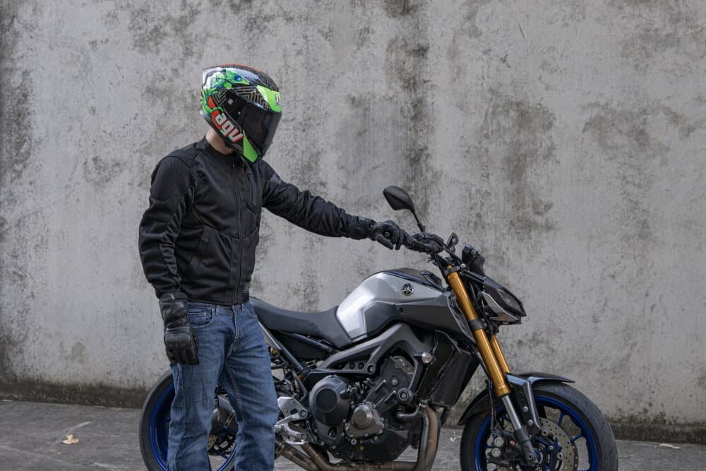 Motorcyclist in AGV helmet and mesh jacket standing beside a Yamaha MT-09 naked bike against a concrete wall