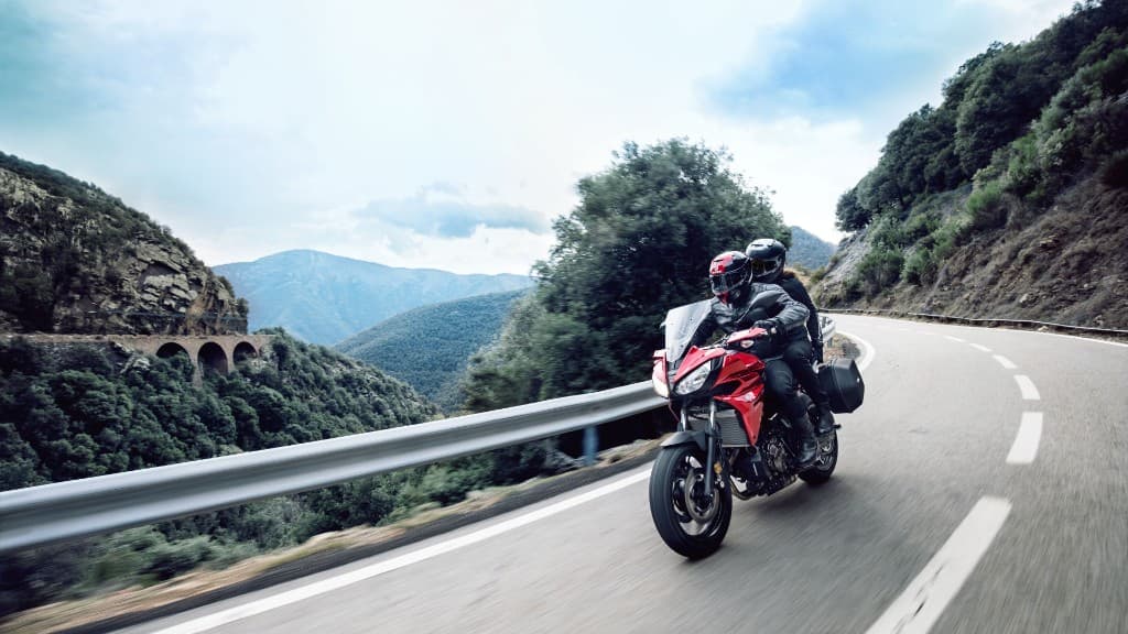 Two riders on a red sport-touring motorcycle with panniers riding along a winding mountain road in NSW