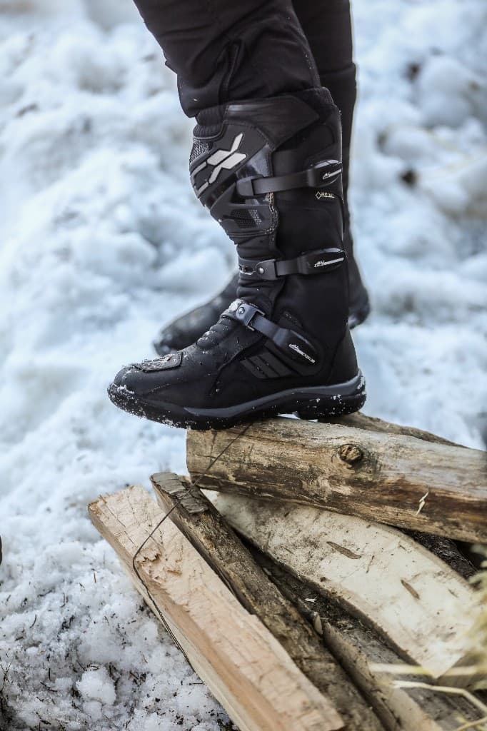 Alpinestars Gore-Tex waterproof motorcycle boots standing on snow-covered logs in winter conditions