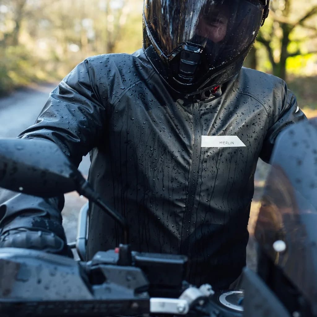 Motorcycle rider wearing a Merlin waterproof jacket covered in rain droplets on a country road